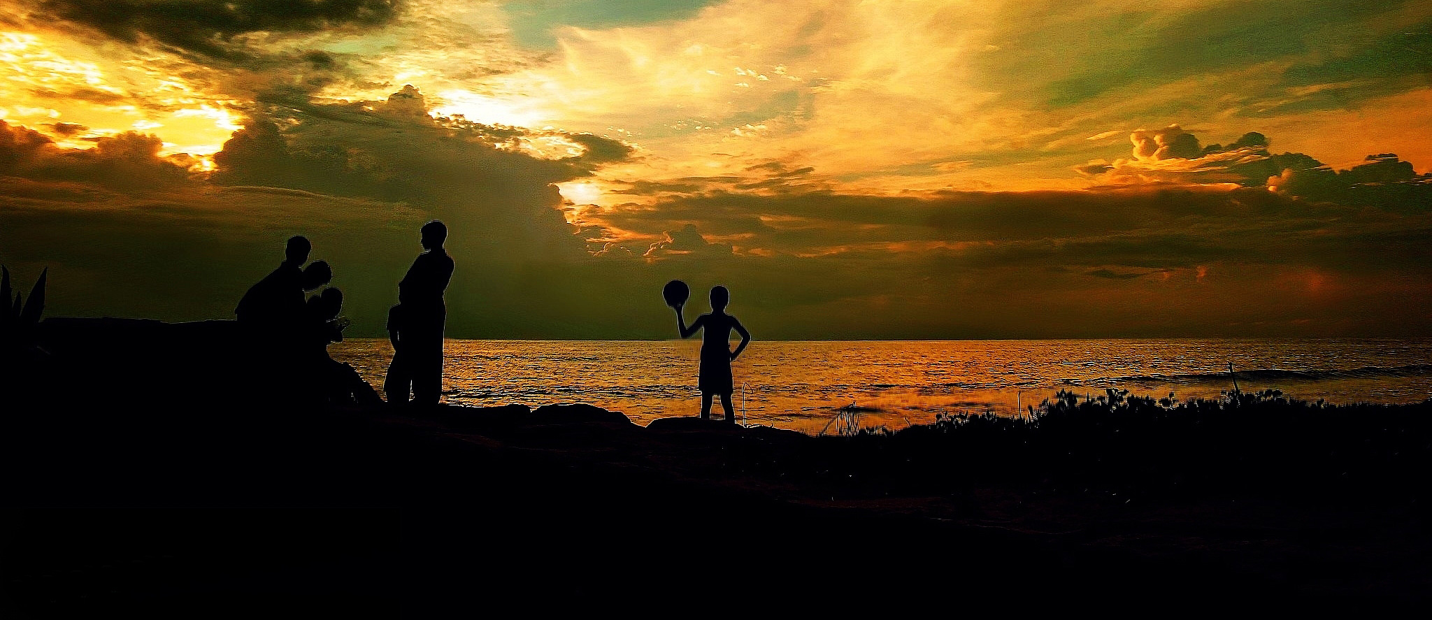 Silhouettes of people playing football at sunset