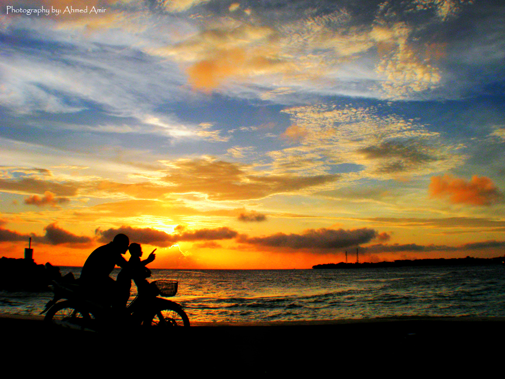 Silhouette of two people on bikes in front of a sunset in Maldives